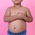 Obese boy who is overweight on a pink background.